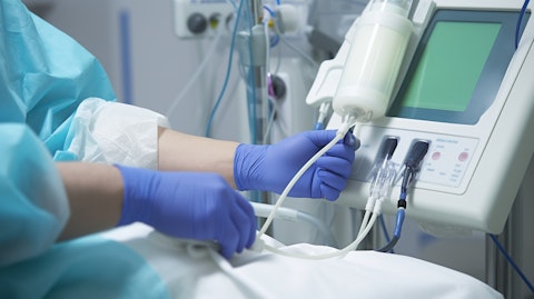 A medical professional in a white coat and gloves administering dialysis treatment to a patient.