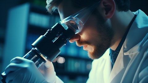 Close up of a scientist wearing a lab coat and safety glasses, examining a sample under the microscope.