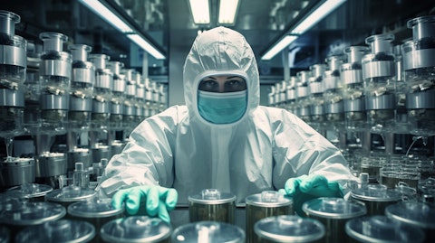 A worker in a cleanroom suit surrounded by pharmaceutical containers.