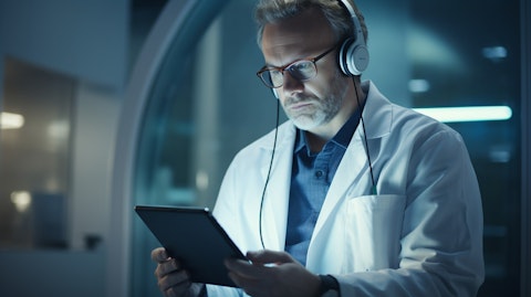 A telehealth professional in a lab coat wearing a headset and talking to a patient through a tablet.