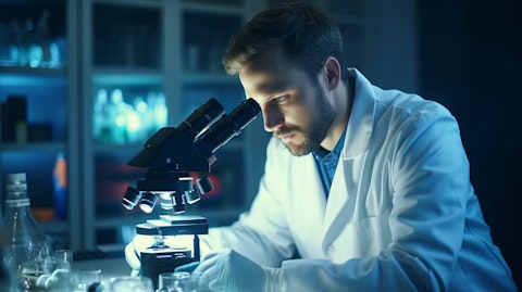 A biomedical laboratory with a molecular biologist wearing a lab coat studying test samples under a microscope.