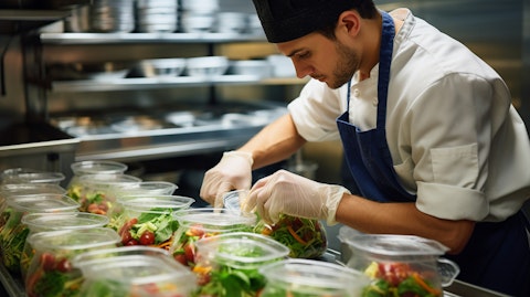 A chef in a restaurant kitchen carefully assembling a meal with fresh ingredients served in plastic and biopolymer-based containers.