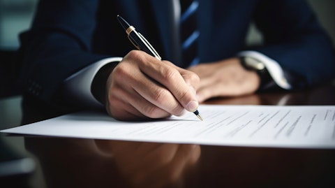 A close up of a businessperson's hand holding a pen as they sign papers contained in a stack on the desk, illustrating the completion of a financial transaction.