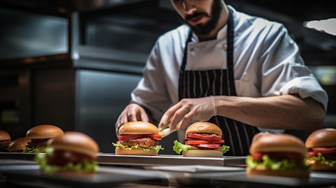 A chef giving final touches to plated burgers in the kitchen.