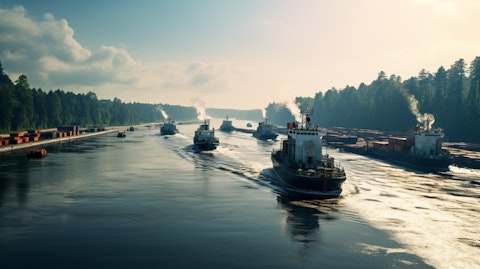 A line of coal-filled barges with a tugboat escorting them down a river, towards a distant port.