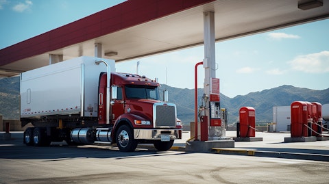 A truck parked at a gas station, its fuel tank being filled from a pump.