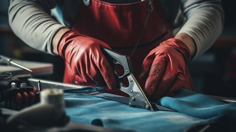 A close-up of a person wearing protective gloves using a pair of scissors in a workshop.