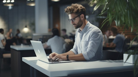 A software developer typing on a laptop in a modern office environment.