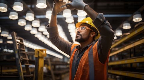 A person wearing a hardhat and safety glasses in a factory installing a LED high bay fixture.