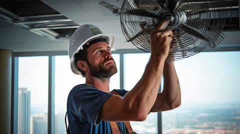 A construction worker in safety gear installing a ceiling fan in a high-rise building.
