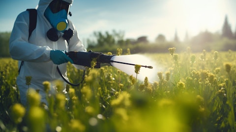 Close-up of a worker wearing protective gear spraying pesticide on a field.